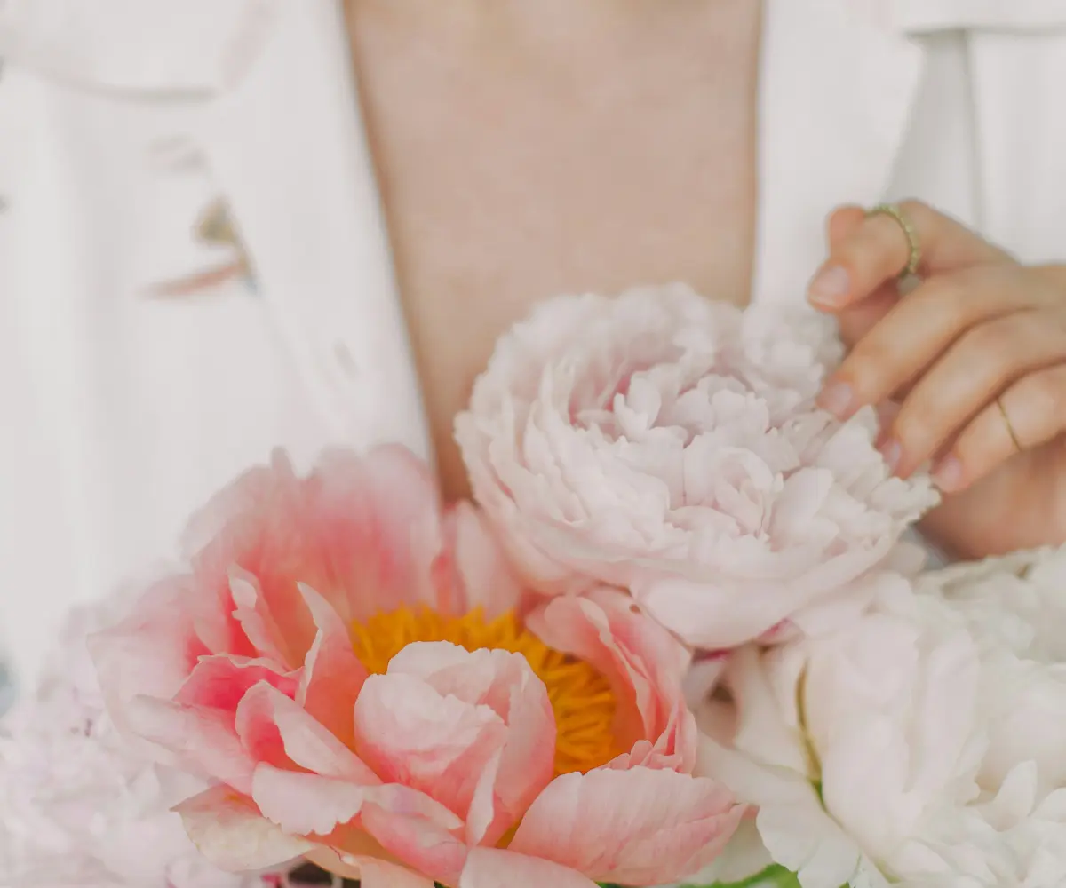 stylish girl in white floral shirt gently holding peonies flowers in hands with jewelry