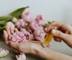 a woman holding a bottle of oil in her hands next to flowers