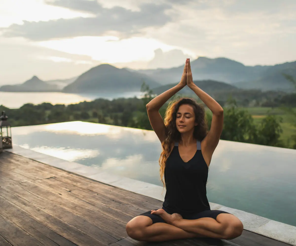 woman meditating alone on infinity poolside with beautiful ocean and mountain view in morning