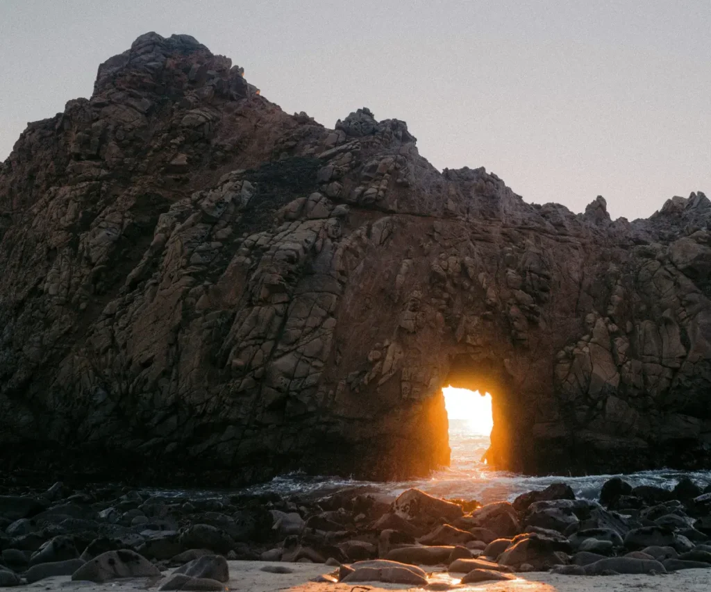 The sun shining through a rock in the sea.